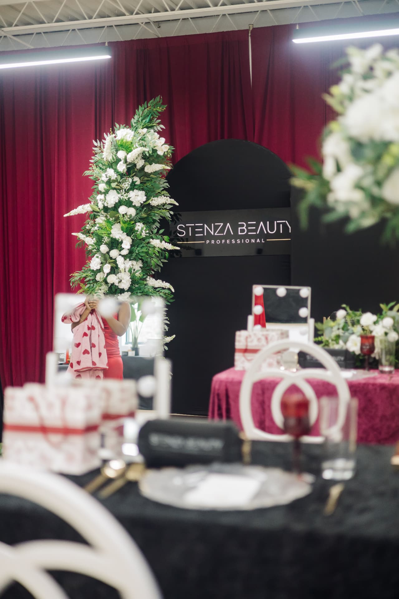 Host carrying a heart-patterned towel past a floral installation at a brand event